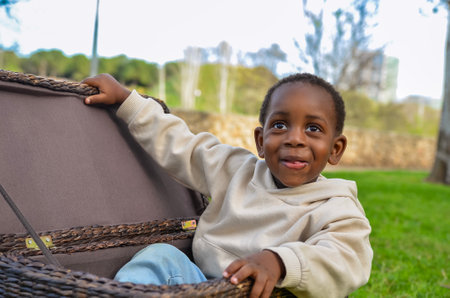 Curious black child sits in a wicker basket in a park, exploring its contents and enjoying the outdoorsの写真素材