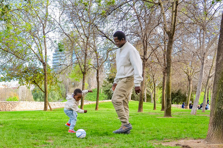 Father teaching his son how to play soccer in a beautiful park, creating lasting memoriesの写真素材