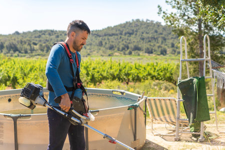 Gardener working with brushcutter near a swimming pool in a sunny settingの写真素材