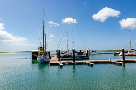 Sailboats and motorboats moored to a pier on a sunny day with blue sky and cloudsの写真素材