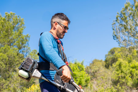 Gardener using a brushcutter is working in a sunny day