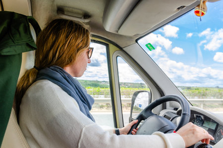 Woman driving a van on a country road, enjoying the sunny landscapeの写真素材