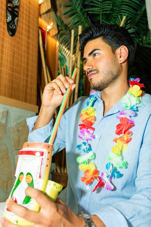 Tourist wearing hawaiian flower necklace drinking a colorful cocktail in a tiki bar
