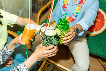 Friends toasting colorful tropical tiki cocktails at a Hawaiian themed party