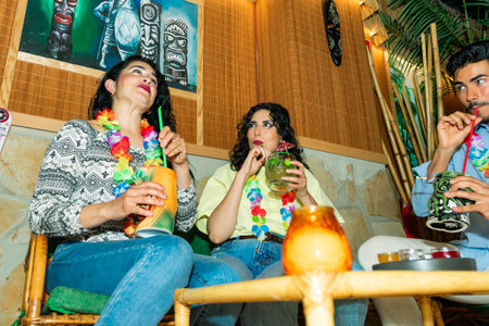 Three friends are relaxing and enjoying colorful, tropical cocktails in a tiki bar