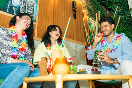 Young adults wearing hawaiian leis are laughing and enjoying drinks in a polynesian-themed barの写真素材