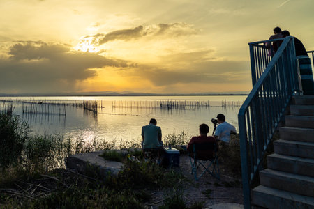 Photographers capturing stunning sunset views over the serene waters of Albufera Natural Park, a beautiful lagoon near Valencia, Spainの写真素材