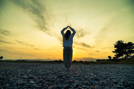 Woman doing yoga on a rocky beach during a stunning sunsetの写真素材