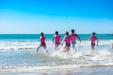 Lifeguards wearing pink and teal uniforms running into the ocean during a summer training exerciseの写真素材