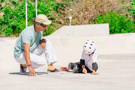 Instructor showing trick to young skater wearing helmet and protective gear in skate parkの写真素材