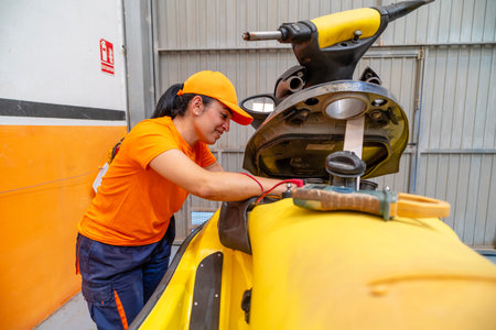 Female mechanic using multimeter testing battery charge of personal watercraft in repair shopの写真素材
