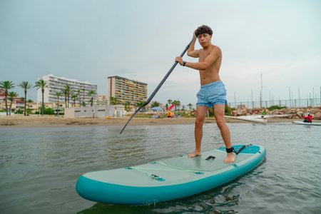 Tourist practicing stand up paddle surfing in the sea near urban beach
