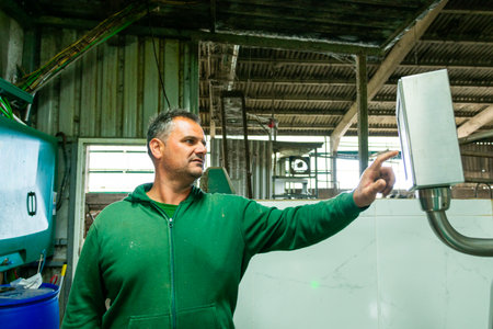 Farmer operating milking machine with digital control panel in barn, showcasing modern dairy farm managementの写真素材