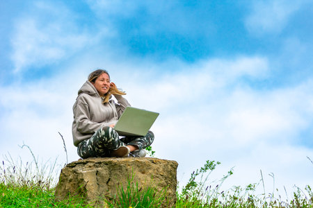 Freelancer working remotely with laptop sitting on a rock in nature enjoying freedom and fresh airの写真素材