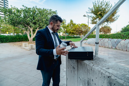 Confident businessman opens his briefcase while holding a coffee cup outsideの写真素材