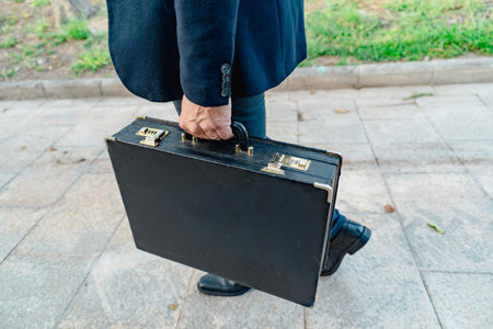 Man in formal suit holds black briefcase while walking on city pavement outdoorsの写真素材