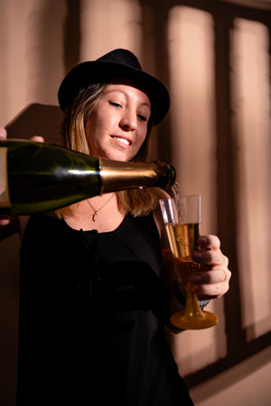 Young woman in hat celebrating, pouring champagne into a flute