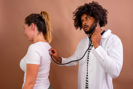Doctor listening to patient's lungs with a stethoscope, performing a health examination for diagnosisの写真素材