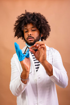 Black doctor putting on a protective medical glove and face maskの写真素材