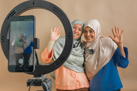 Two smiling muslim women creating online video content with a ring light and smartphone