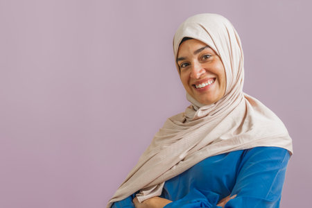 Smiling young woman wearing a hijab and blue shirt posing confidently with arms crossedの写真素材