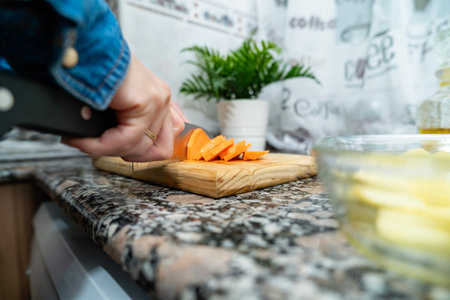 Person's hands preparing sweet potato slices on a wooden cutting board for a healthy mealの写真素材