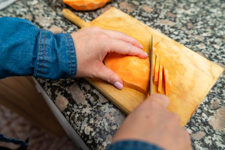 Woman preparing fresh sweet potato slices on a cutting board in a kitchenの写真素材