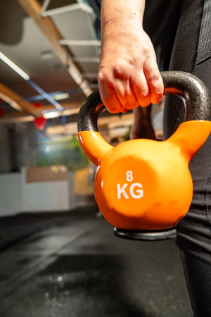 Hand holding an orange 8 kg kettlebell during a workout in a gymの写真素材