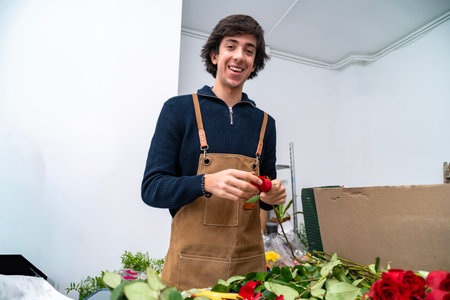 Smiling florist preparing red roses, wearing an apron in a flower shopの写真素材