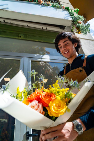 Smiling florist offering colorful fresh flower arrangement outside flower shopの写真素材