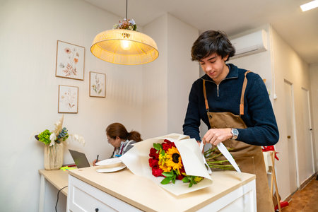 Florist preparing a vibrant bouquet of roses and sunflowers with a white ribbon in a flower shopの写真素材