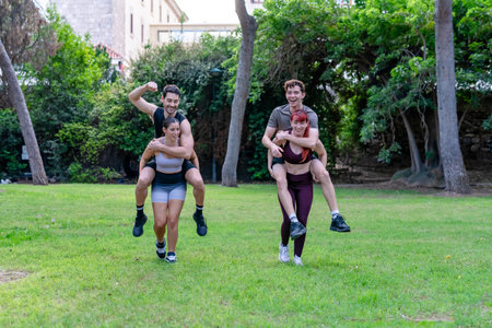 Happy couples having fun piggyback riding on green grass in an outdoor park