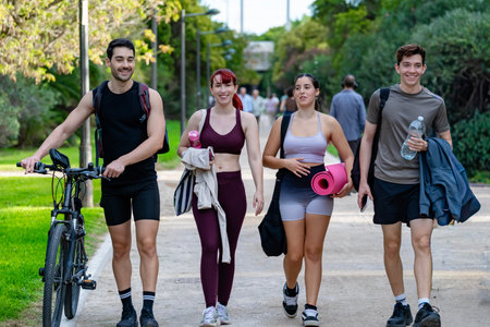 Group of young adults walking together in a park after a fitness session, sharing an active...