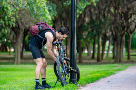 Young man securing his bicycle to a street lamp with a chain lockの写真素材