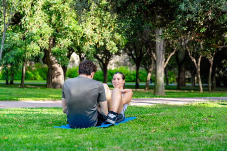 Young man assisting woman with abdominal sit-ups on a mat in a parkの写真素材