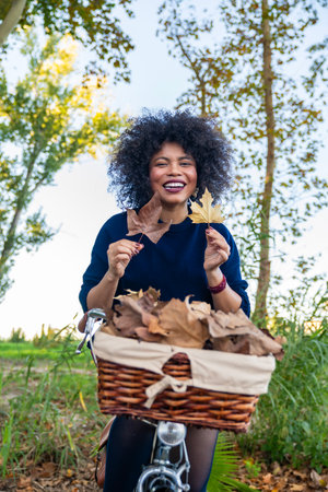Happy woman enjoying fall season outdoors with a bike and basket full of leavesの写真素材