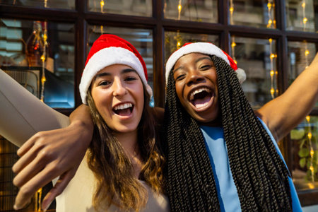 Diverse female friends wearing santa hats laughing together during festive christmas celebrationの写真素材