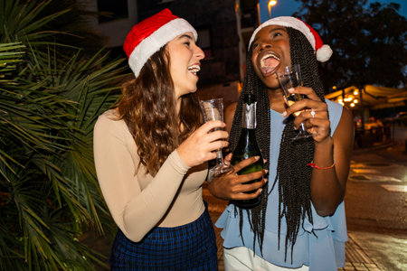 Two laughing friends in santa hats enjoying a festive holiday celebration outdoors at nightの写真素材