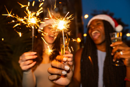 Two diverse women friends joyfully celebrating holiday party with bright sparklers and champagneの写真素材