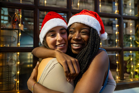 Happy diverse friends wearing santa hats, hugging and celebrating holidays togetherの写真素材