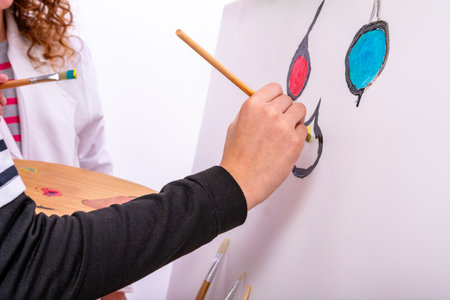 Artist's hand holding a paintbrush adding bright colors to a white canvas