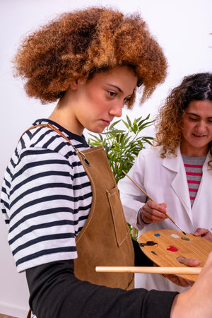 Woman instructor teaching painting skills to a young student with an apron and palette