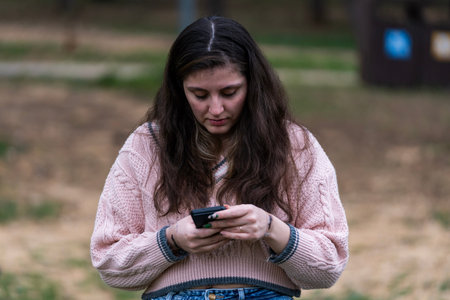 Young woman looking down, concentrated on smartphone in outdoor setting