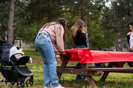 Women arranging a picnic tablecloth in a park while holding a baby, preparing for outdoor leisure