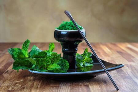 Shisha mint in glossy black cup on a plate with fresh mint leaves
