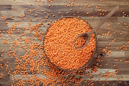 Lentils red in a wooden bowl standing on the kitchen table made of oak. Top view.の写真素材