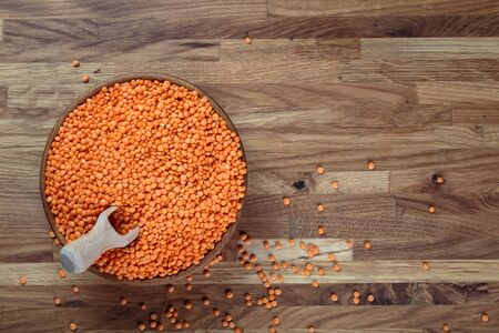 Lentils red in a wooden bowl standing on the kitchen table made of oak. Top view.の写真素材