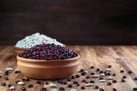 Beans red and white in a wooden bowl standing on the kitchen table made of oak.の写真素材