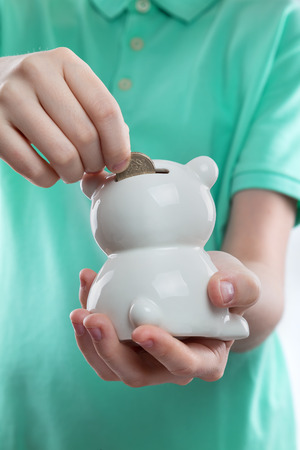 child's hand throwing a coin into a white porcelain piggy bankの写真素材