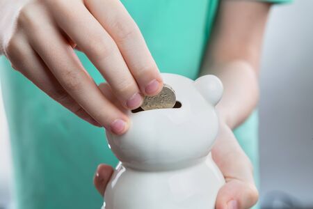 child's hand throwing a coin into a white porcelain piggy bankの写真素材